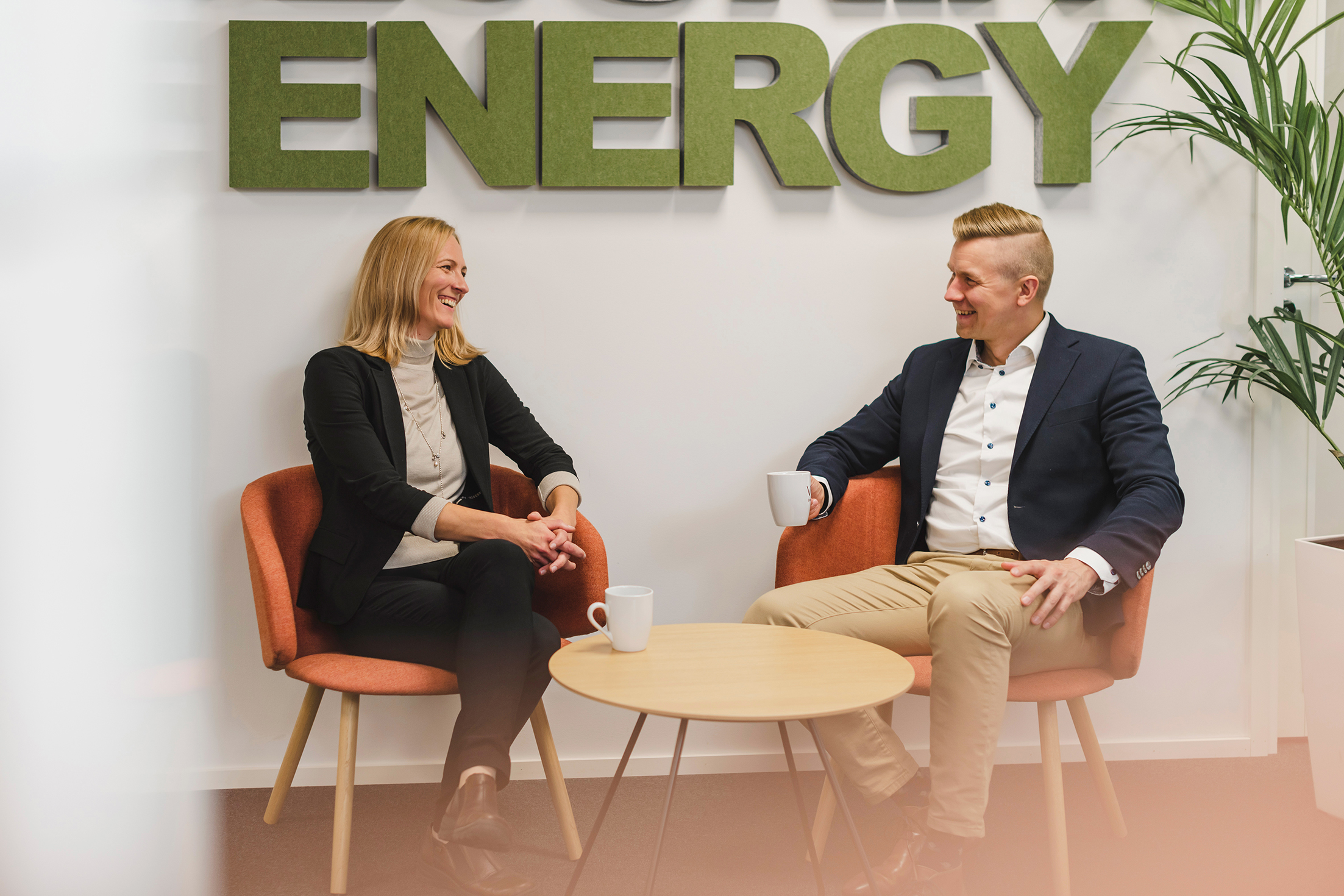Employees Minna Lindholm and Arto Peltola sitting down in front of sign on the wall reading "energy"