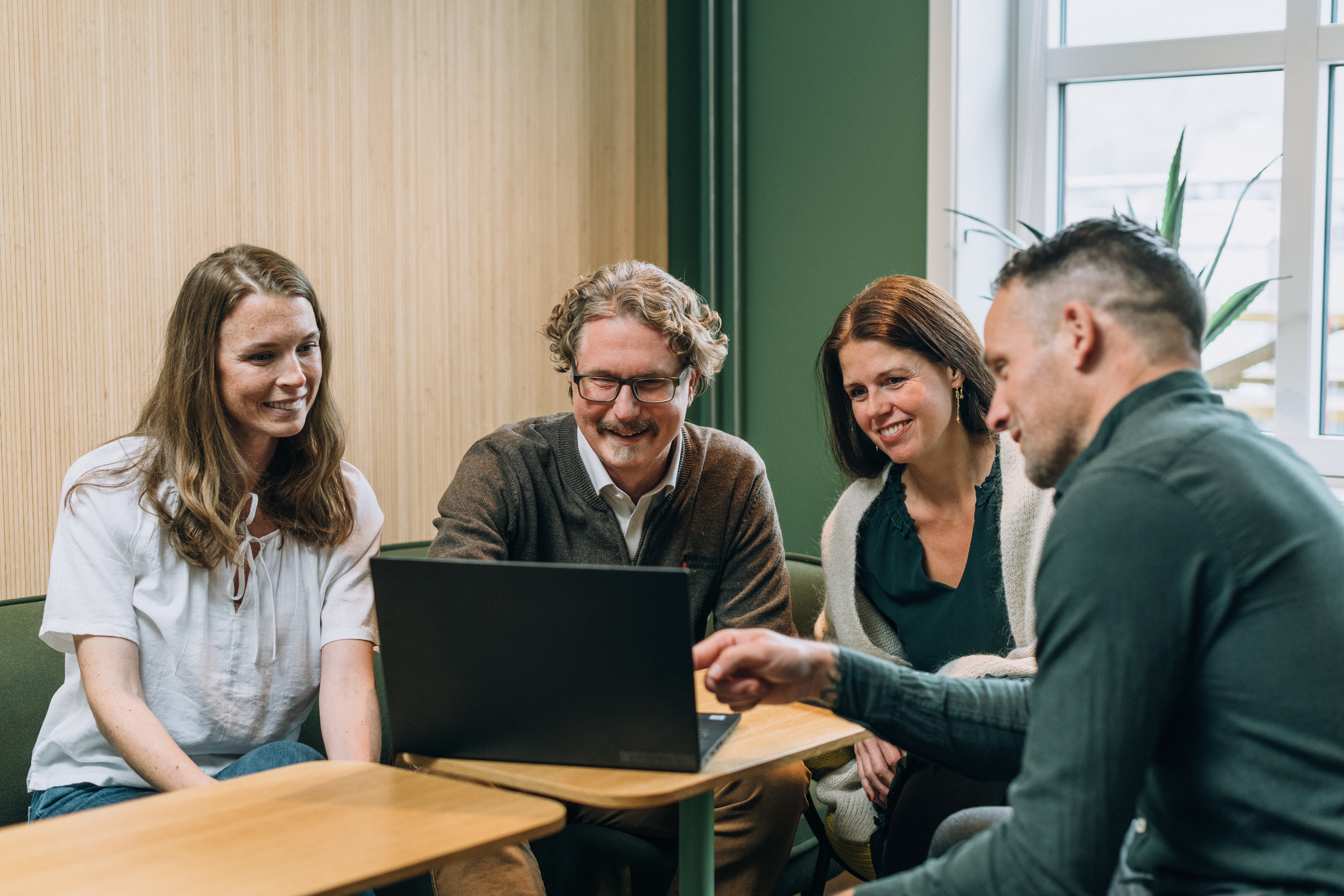 Four employees, two women and two men, gathered around a laptop in an inviting meeting room