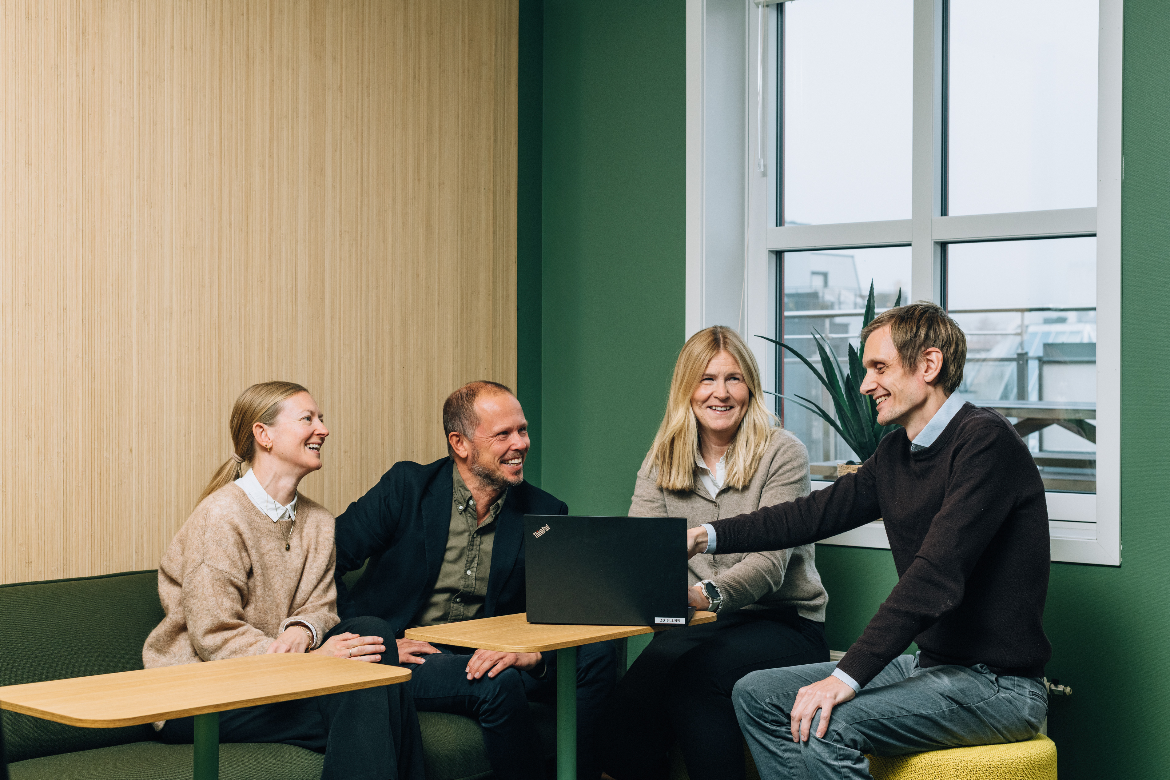 Four employees, two women and two men, gathered around a laptop in an inviting meeting room