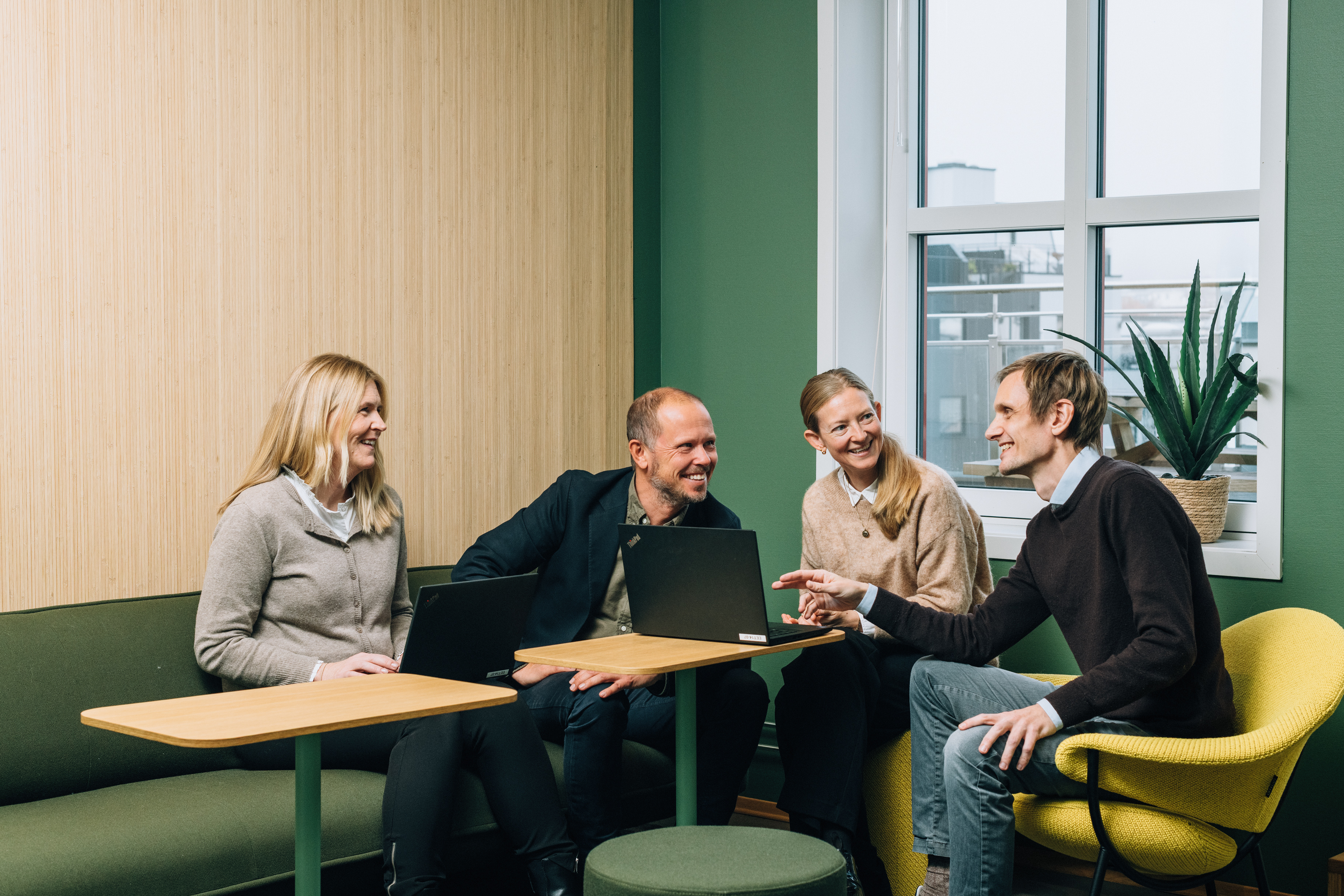 Four employees, two women and two men, gathered around a laptop in an inviting meeting room