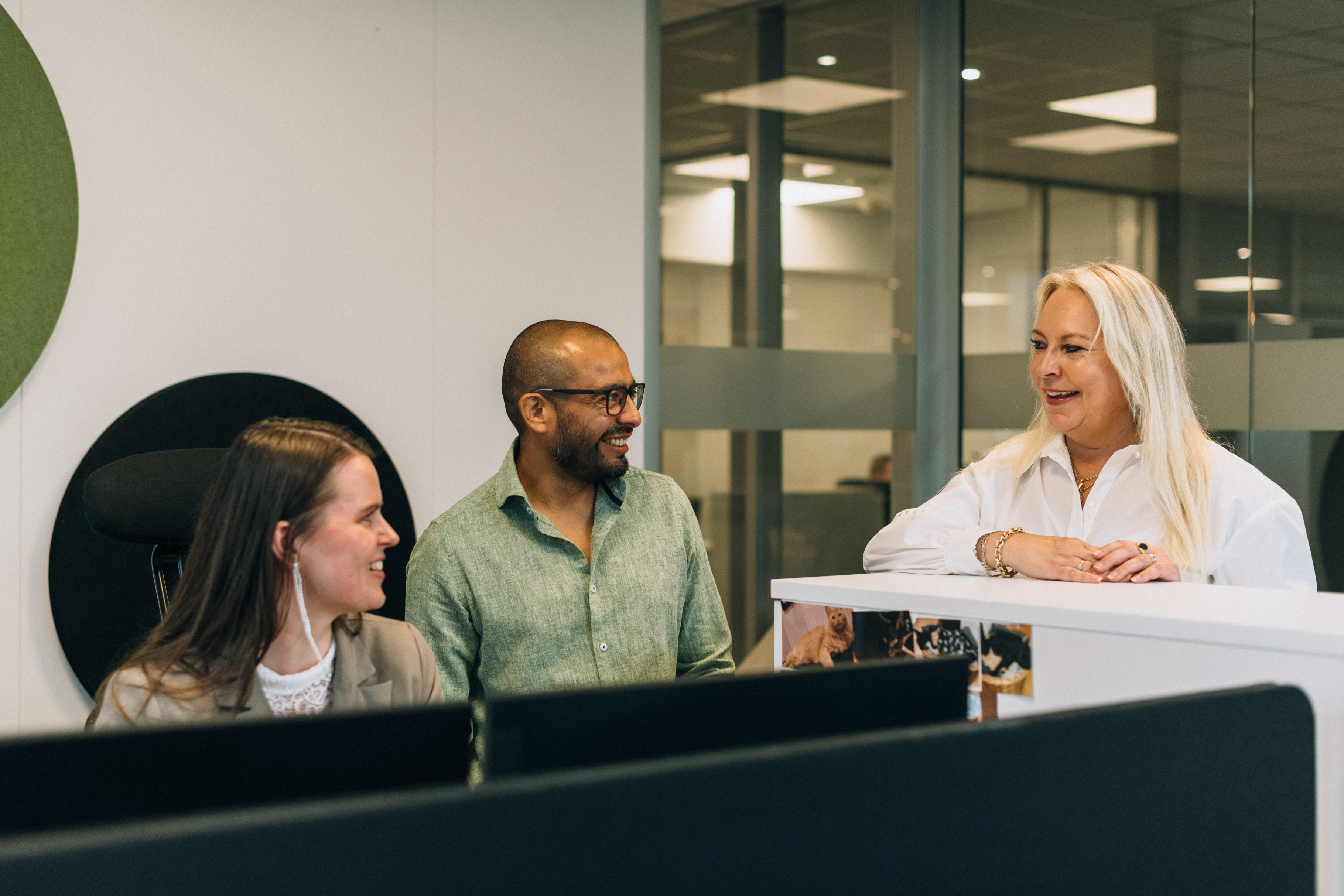 Employees Cecilie, Vegard and Britt having a chat with Cecilie who is seated behind her desk