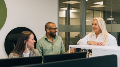Employees Cecilie, Vegard and Britt having a chat with Cecilie who is seated behind her desk