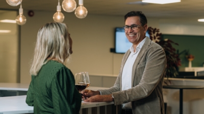 A female employee seen from the back speaking to employee Trond Lutdal in a bar setting with hanging lightbulbs overhead