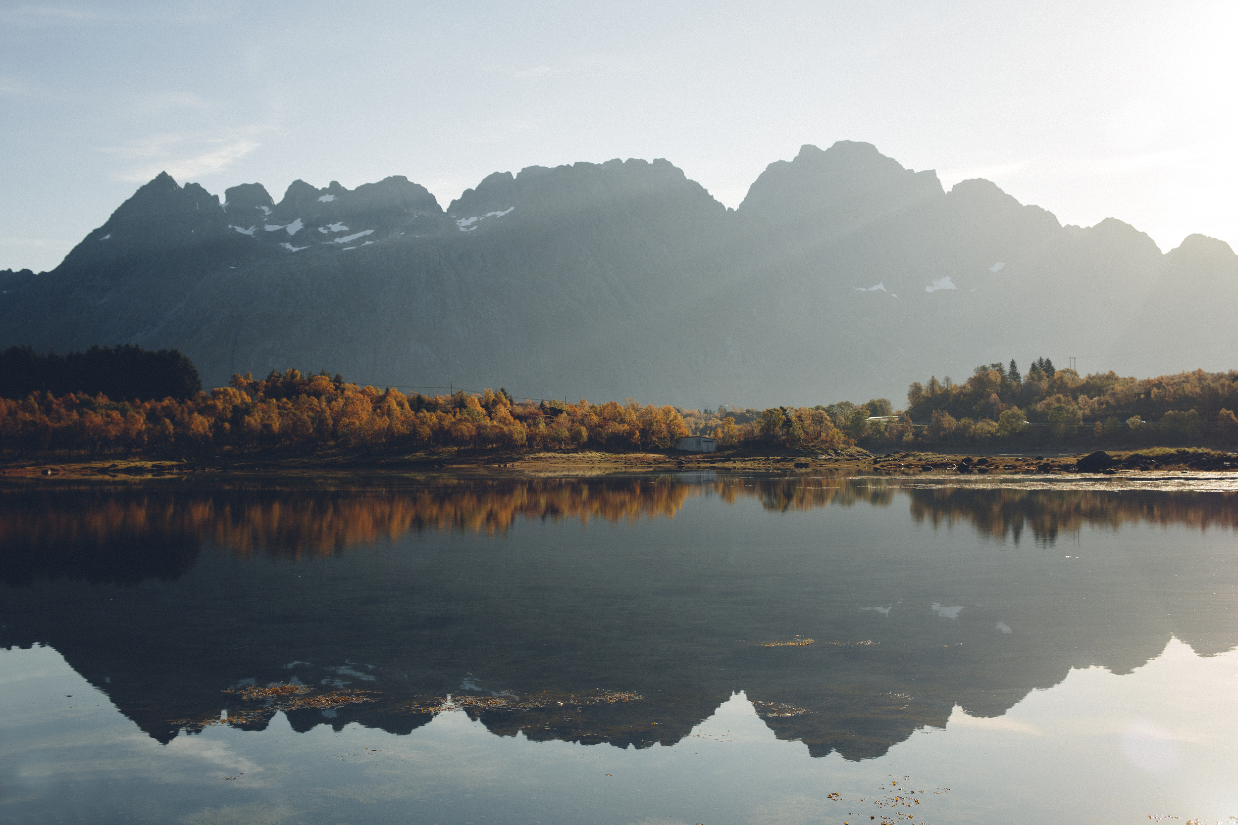 A treeline with autumn colours meets the lake in the middlem with a large mountain in the distance, both reflected in the lake