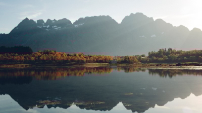 A treeline with autumn colours meets the lake in the middlem with a large mountain in the distance, both reflected in the lake