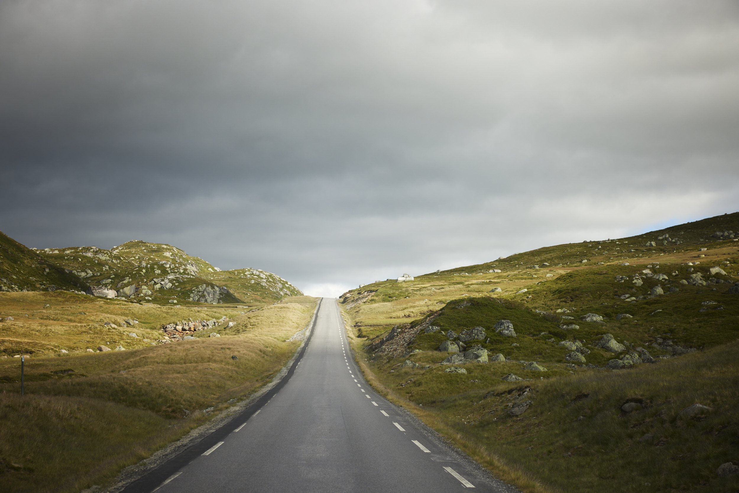 A horizon line in the middle where a road meets grey skies, with sun in the distance