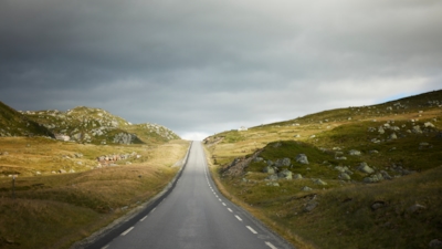 A horizon line in the middle where a road meets grey skies, with sun in the distance